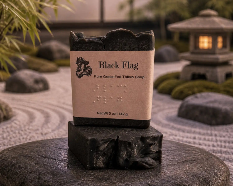 Black Flag tallow soap bars stacked in a Zen garden with raked gravel and stone lantern. Blind Pirate Trading Co.