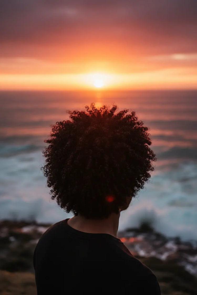 Natural Afro Male watching the sun fall behind the ocean horizon. very healthy hair.