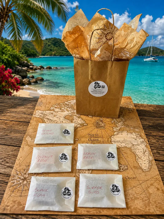 Stowaway Discovery Set flat lay — five  glassine-wrapped soap samples with gift bag and pirate tissue paper.
