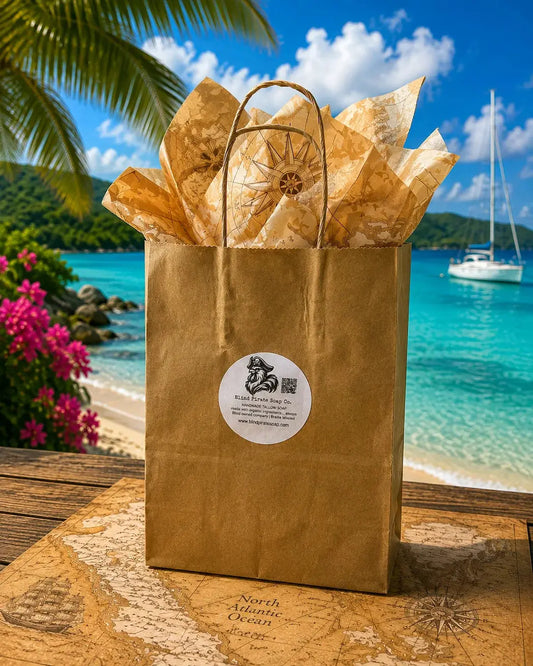 Blind Pirate Trading Co. Stowaway Discovery Set kraft gift bag with tissue paper on a tropical beach, turquoise water and sailboat behind