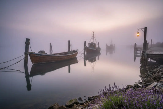 Misty dawn harbor, wooden boats moored in still purple water, lantern glowing on the dock. Blind Pirate Trading Co.