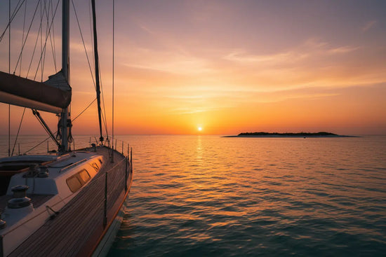 Golden Hour at Anchor — a sailboat  rests calmly at anchor, a warm orange sun melting behind a silhouetted island in the fading dusk.